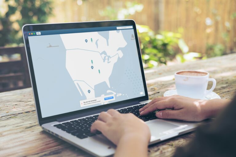 Person using laptop showing a location map on wood table with coffee